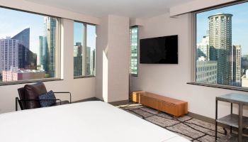 A modern hotel room with a bed, wall-mounted TV, chair, and city skyline view from large windows ends the sentence.