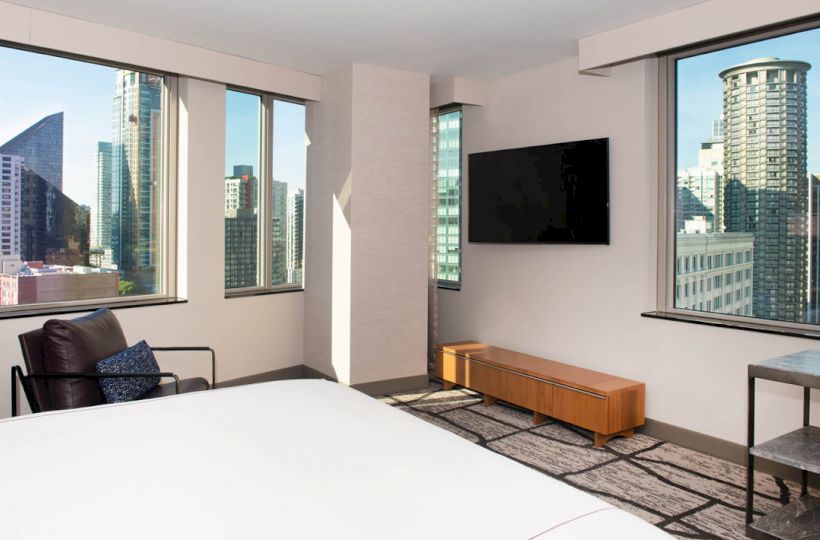 A modern hotel room with a bed, wall-mounted TV, chair, and city skyline view from large windows ends the sentence.