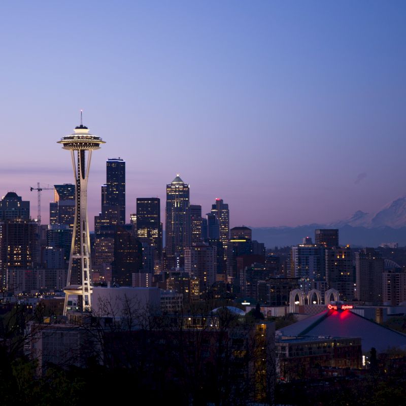 This image shows the Seattle skyline at dusk, featuring the Space Needle prominently with Mount Rainier in the background.