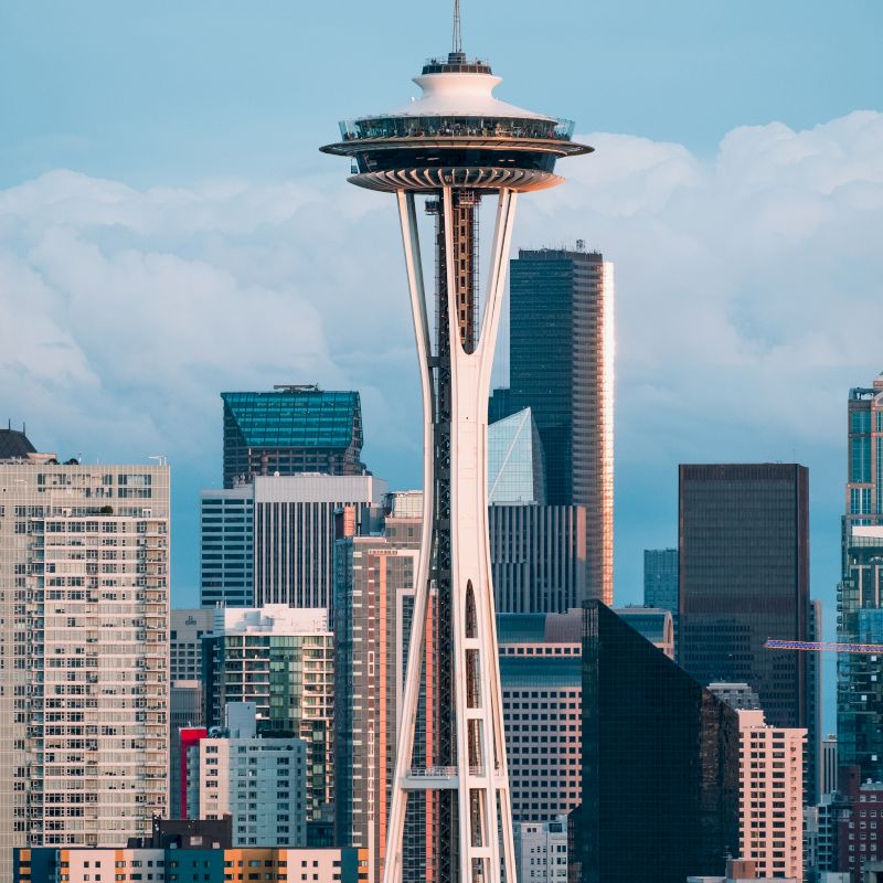 The image features the Space Needle with a backdrop of tall skyscrapers and a partly cloudy sky, showcasing a striking cityscape.